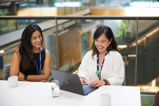 two females in a meeting looking at work on laptop and smiling